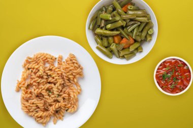 Domates soslu beyaz tabakta makarna ve sebze salatası.