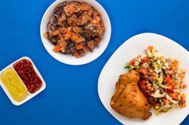 Kızarmış tavuk butları ve sebzeler beyaz tabakta.