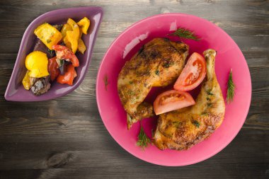 Siyah ahşap arka planda sebzeli tavuk budu. Tavuk budu pembe tabakta, sebze salatası manzaralı.