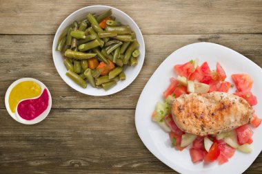 Domates salatası, salatalık ve soğanlı ızgara tavuk göğsü. Ahşap arka planda beyaz bir tabakta ızgara tavuk göğsü. Kızarmış tavuk göğsü manzaralı. Düz yatıyordu.