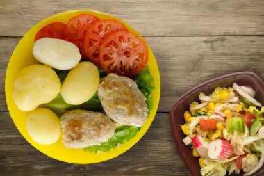 Sarı tabakta patates ve sebze salatası manzaralı pirzola. Kahverengi ahşap arka planda patatesli pirzola
