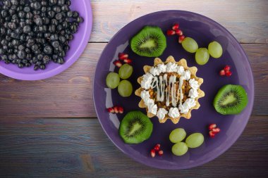 Kek ve meyve üzümleri, kivi, mor ahşap arka planda nar. Mor tabak manzaralı tatlı.