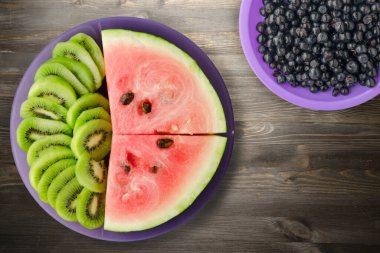Karpuz ve kivi siyah ahşap bir zemin üzerinde mor bir tabakta dilimlendi.