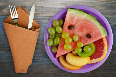 Mavi ahşap arka planda dilimlenmiş meyve. Kesilmiş meyve, mor bir tabakta, çatal ve bıçak.