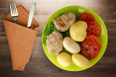 Kireç tabağında patates ve çatal ve bıçak manzaralı pirzola. Kahverengi ahşap arka planda patatesli pirzola