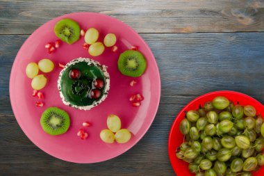 Kek ve meyve üzümleri, kivi, mavi ahşap zemin üzerinde nar. Tatlı pembe bir tabakta.