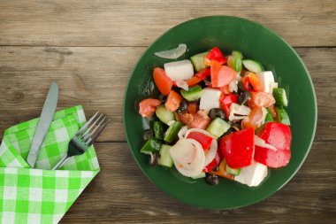 Kahverengi ahşap arka planda Yunan salatası. Çatal ve bıçak manzaralı yeşil tabakta Yunan salatası. sağlıklı yiyecekler