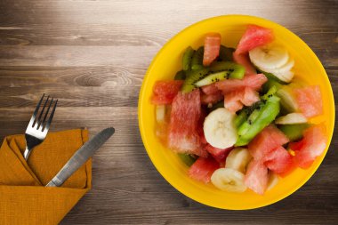 Kahverengi ahşap arka planda sağlıklı taze meyve salatası tabağı. Çatallı ve bıçak manzaralı meyve salatası.