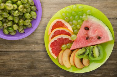 Doğuştan ahşap arka planda kesilmiş meyve. Açık yeşil bir tabakta dilimlenmiş meyve ince zeka meyveleri mor bir tabakta.