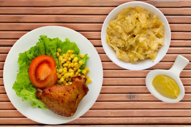 Beyaz tabakta marul, mısır ve domatesli tavuk kanadı. Sebze salatalı tavuk kanadı ve turuncu ahşap arka plan manzaralı sos.