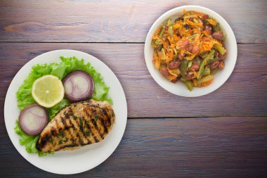 Sebzeli ızgara tavuk fileto limon, salata, mor ahşap arka planda soğan. Tavuklu fileto, beyaz tabak şeklinde ızgara.