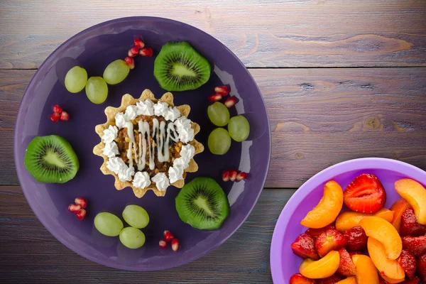 Kek ve meyve üzümleri, kivi, mor ahşap arka planda nar. Mor tabak manzaralı tatlı.