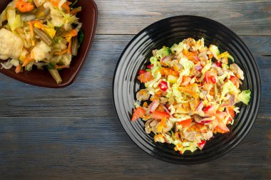 Tavuk mideli salata ile sebze havuç, soğan, biber, lahana, domates, brokoli. Mavi ahşap arka planda siyah tabakta tavuklu salata. Vejetaryen salata üstü görünümü.