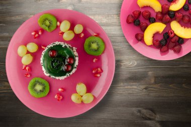 Kek ve meyve üzümleri, kivi, siyah ahşap zemin üzerinde nar. Pembe tabakta meyveli tatlı.