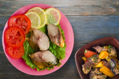 Sebze salatası manzaralı pembe tabakta tütsülenmiş uskumru. Mavi ahşap arka planda limonlu uskumru ve domates.