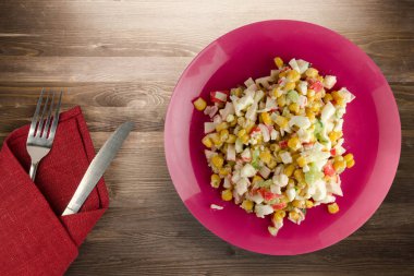 Çatal ve bıçak manzaralı kırmızı tabakta yengeç salatası. Kahverengi ahşap arka planda yengeç salatası