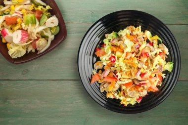 Tavuk mideli salata ile sebze havuç, soğan, biber, lahana, domates, brokoli. Yeşil ahşap arka planda siyah tabakta tavuklu salata.