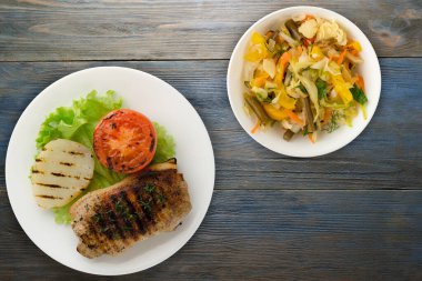 Mavi ahşap arka planda patates ve domatesle ızgara domuz eti. Salata soslu ızgara domuz eti.