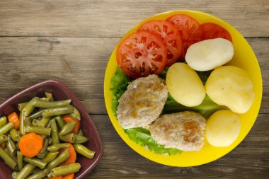 Sarı tabakta patates ve sebze salatası manzaralı pirzola. Kahverengi ahşap arka planda patatesli pirzola