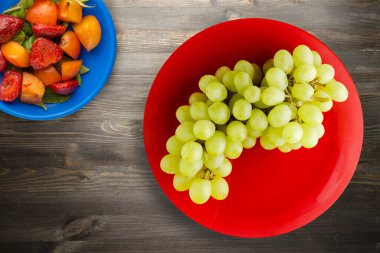 Siyah ahşap arka planda üzümler. Kırmızı tabakta üzümler. Sağlıklı vejetaryen yemekleri.