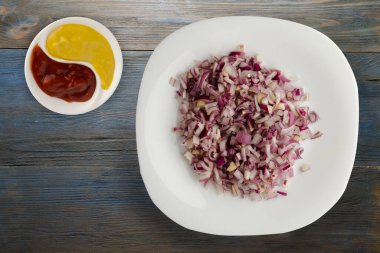 Mavi gri ahşap arka planda kırmızı soğan. Beyaz tabakta doğranmış kırmızı soğan ve soslu üst görünüm.