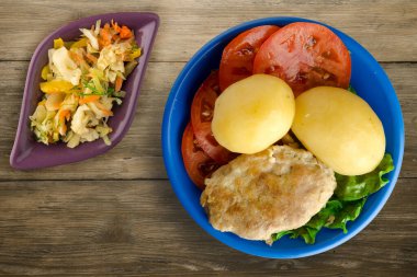 Mavi tabakta patates ve sebze salatası manzaralı pirzola. Tahta arka planda patatesli pirzola.