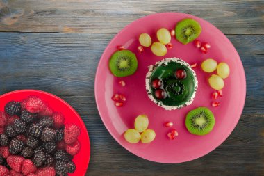 Kek ve meyve üzümleri, kivi, mavi ahşap zemin üzerinde nar. Tatlı pembe bir tabakta.