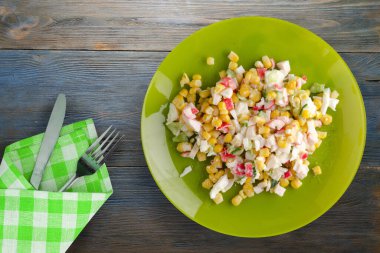 Kireç tabağında çatal ve bıçaklı yengeç salatası. Mavi gri ahşap arka planda yengeç salatası.