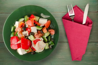 Yeşil ahşap arka planda Yunan salatası. Çatal ve bıçak manzaralı yeşil tabakta Yunan salatası. sağlıklı yiyecekler