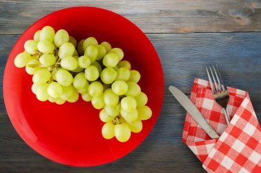 Mavi ahşap arka planda üzümler. Çatal ve bıçak manzaralı kırmızı bir tabakta üzümler.