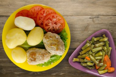 Sarı tabakta patates ve sebze salatası manzaralı pirzola. Kahverengi ahşap arka planda patatesli pirzola
