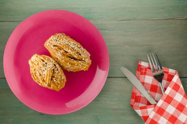 Çatal ve bıçak manzaralı pembe bir tabakta susam tohumlu kekler. Yeşil ahşap arka planda susam tohumlu kekler