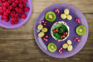 Kek ve meyve üzümleri, kivi, ahşap zemin üzerinde nar. Mor bir tabakta meyveli tatlı.