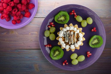 Kek ve meyve üzümleri, kivi, mor ahşap arka planda nar. Mor tabak manzaralı tatlı.