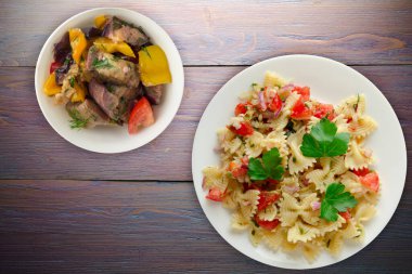 Beyaz tabakta makarna. Mor ahşap arka planda makarna, soğan, lahana. Vejetaryen salata soslu makarna.