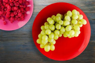 Mavi ahşap arka planda üzümler. Meyve salatası manzaralı kırmızı bir tabakta üzümler