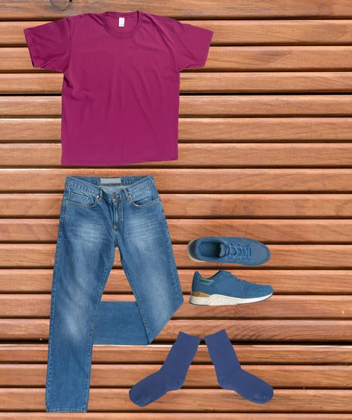 flat lay, men\'s fashion.blue jeans ,blue sneakers,red t-shirt,dark blue socks on a wooden background. casual clothes top view