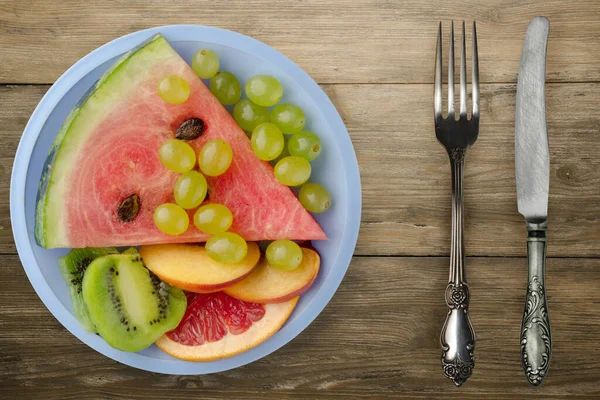 茶色の木の背景にフォークとナイフで果物をスライス 薄緑色のプレートの上から見たフルーツのスライス — ストック写真