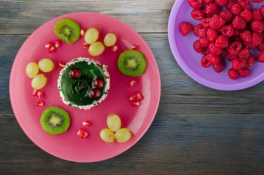 Kek ve meyve üzümleri, kivi, mavi ahşap zemin üzerinde nar. Tatlı pembe bir tabakta.