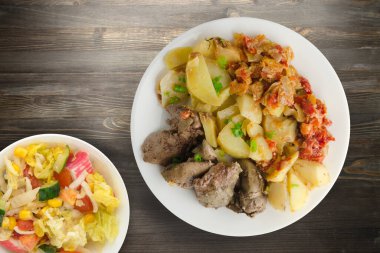 Patatesli kızarmış ciğer ve sebze salatalı haşlanmış domates. Siyah ahşap arka planda beyaz tabakta kızarmış ciğer.
