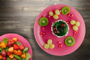 Kek ve meyve üzümleri, kivi, siyah ahşap zemin üzerinde nar. Pembe tabakta meyveli tatlı.