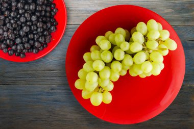 Mavi ahşap arka planda üzümler. Meyve salatası manzaralı kırmızı bir tabakta üzümler