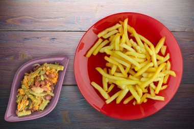 Ahşap arka planda patates kızartması. Kırmızı tabakta patates kızartması ve vejetaryen salatası.