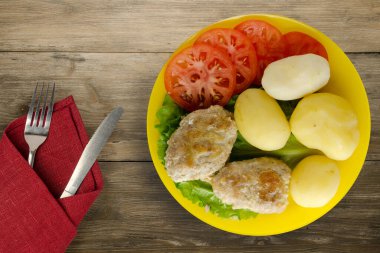 Çatal ve bıçak manzaralı sarı tabakta patatesli pirzola. Kahverengi ahşap arka planda patatesli pirzola