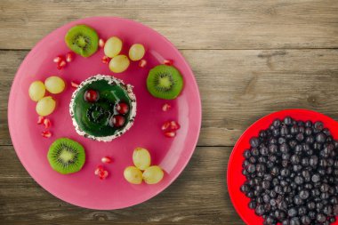 Kek ve meyve üzümleri, kivi, ahşap zemin üzerinde nar. Meyveli tatlı pembe tabak manzaralı.