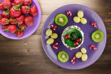 Kek ve meyve üzümleri, kivi, kahverengi ahşap zemin üzerinde nar. Mor tabak manzaralı meyveli tatlı.