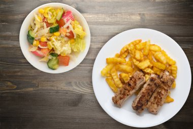 Beyaz tabakta domuz kaburgası ve patates, sebze salatası ve siyah ahşap arka planda sos. Fast food 'un en iyi manzarası. Sağlıksız yiyecekler.