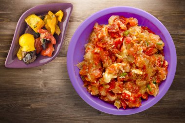 Kahverengi ahşap arka planda mor tabakta soğanlı haşlanmış domatesler. Soğan manzaralı haşlanmış domates. Sebze salatalı vejetaryen yemeği