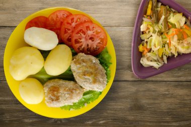 Sarı tabakta patates ve sebze salatası manzaralı pirzola. Kahverengi ahşap arka planda patatesli pirzola