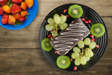 Kek ve meyve üzümleri, kivi, ahşap zemin üzerinde nar. Meyve manzaralı siyah tabakta tatlı.